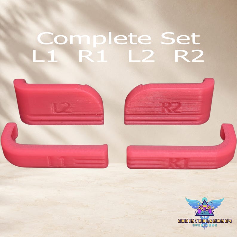 May include: A complete set of four pink controller bumper and trigger buttons labeled L1, R1, L2, and R2. The components feature a textured surface with embossed lettering and are arranged in two rows. The text Complete Set L1 R1 L2 R2 is visible above the buttons.