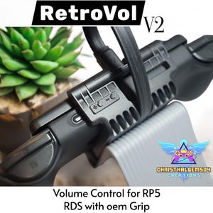 May include: A black RetroVol V2 volume control for RP5 RDS with oem Grip. The device has a series of buttons and a strap. The text "RetroVol" is at the top, and "Volume Control for RP5 RDS with oem Grip" is at the bottom.
