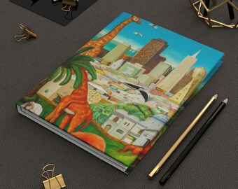 May include: A colorful notebook with a giraffe and cityscape illustration. The cover features a giraffe standing in front of a city skyline with buildings, palm trees, and a blue sky.