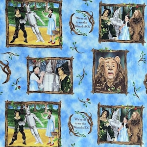 May include: A blue fabric with a repeating pattern of framed images from The Wizard of Oz. The images feature Dorothy, the Scarecrow, the Tin Man, and the Cowardly Lion. The text "We're off to see the Wizard of Oz" is included in the pattern.