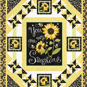 May include: A quilt with a black and white background featuring a yellow sunflower with the text "You are my Sunshine" in white. The quilt is surrounded by a border of yellow sunflowers and black bees.