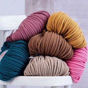 May include: A stack of five different colored cotton rope yarn skeins. The colors are teal, beige, brown, mustard yellow, and pink.