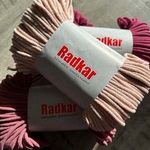 May include: Two spools of cotton cord, one pink and one burgundy, with the label "Radkar Sznurek Bawelniany" on the pink spool.