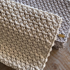 May include: Two rectangular items crafted from thick, cream and light beige cord woven in a dense, interlocking pattern. Each piece features a small, oval-shaped wooden tag attached to the corner, clearly engraved with the text OV Cords.