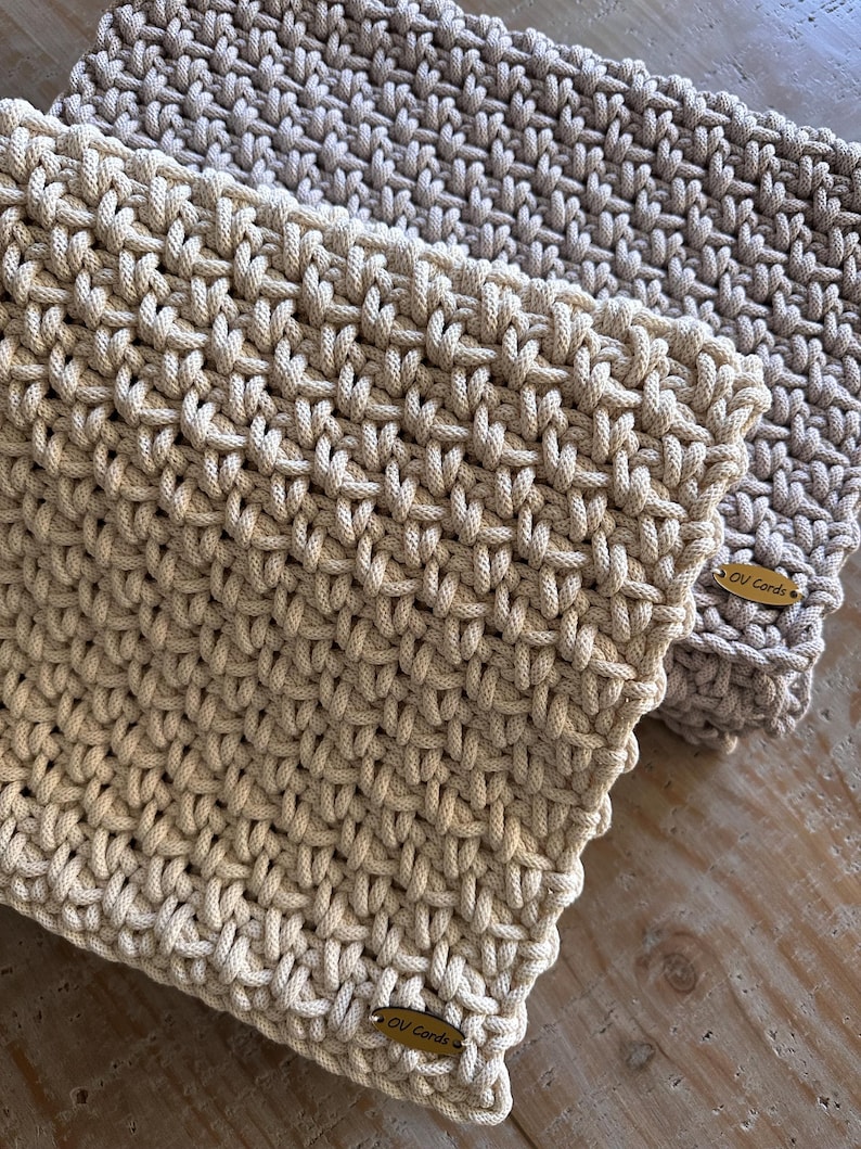May include: Two rectangular items crafted from thick, cream and light beige cord woven in a dense, interlocking pattern. Each piece features a small, oval-shaped wooden tag attached to the corner, clearly engraved with the text OV Cords.