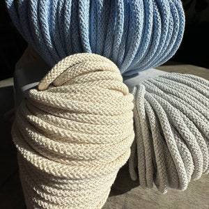May include: Two spools of cotton rope, one in a light blue color and the other in a natural off-white color. The spools are stacked on top of each other.