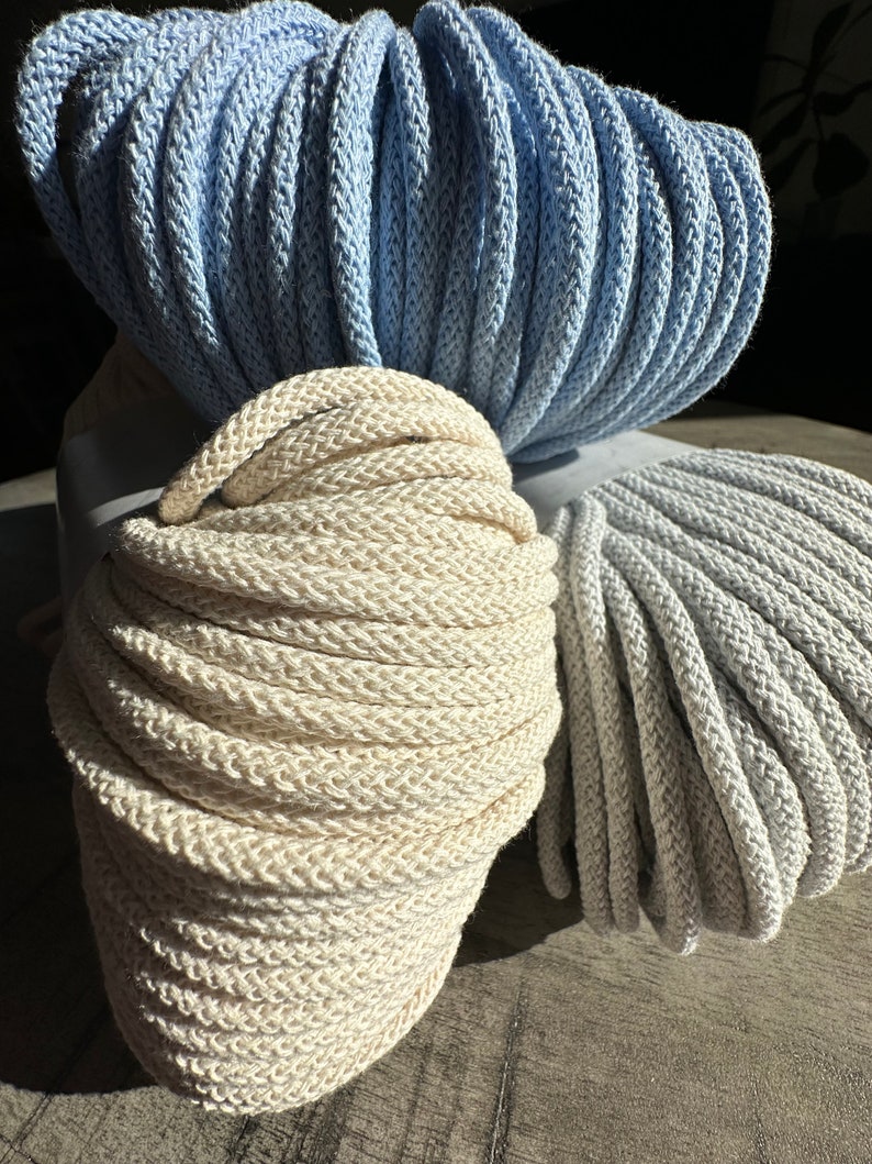 May include: Two spools of cotton rope, one in a light blue color and the other in a natural off-white color. The spools are stacked on top of each other.