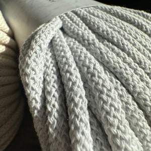 May include: A close-up of a gray cotton rope, wound into a coil. The rope is thick and textured, with a label that reads "Anchor Brand" in red letters.