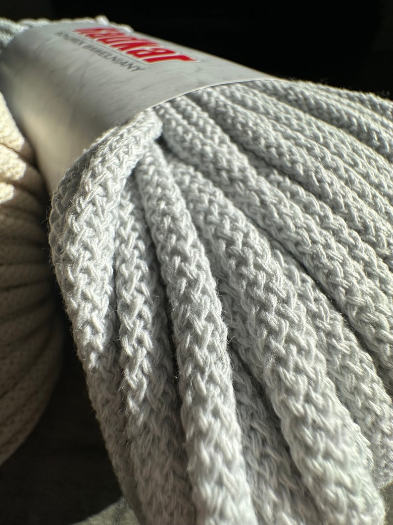May include: A close-up of a gray cotton rope, wound into a coil. The rope is thick and textured, with a label that reads "Anchor Brand" in red letters.