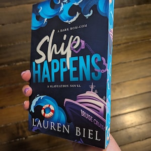 May include: A book titled "Ship Happens" by Lauren Biel. The cover features a dark blue background with white and blue text. A cruise ship illustration is visible, along with a life preserver and waves.