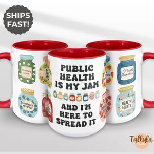 May include: White ceramic mugs with red interiors and handles. The mugs feature colorful illustrations of jam jars and the text "PUBLIC HEALTH IS MY JAM AND I'M HERE TO SPREAD IT". The mugs are decorated with various health-related phrases.