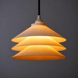 Puede incluir: Una lámpara colgante de tres niveles con una pantalla cónica blanca que presenta un patrón geométrico fino, texturizado y repetitivo. La luz emite un brillo cálido y suave desde el interior, iluminando los detalles de cada capa.