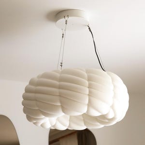 May include: A white pendant light fixture featuring a rounded, cloud-like shape with a soft, segmented, and tufted texture. The light is suspended from a circular white ceiling mount by thin metal wires and includes a black electrical cord.