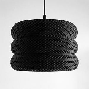 May include: Black pendant light with a woven, cylindrical shade. The shade has a textured, honeycomb-like pattern and is made of multiple layers.