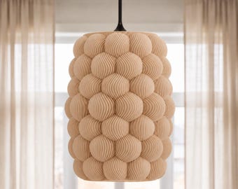 May include: A cylindrical pendant light fixture featuring a textured surface composed of numerous beige, spherical, ribbed elements. The light is suspended from a thin black cord attached to a black conical mount at the top center.