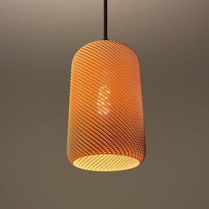 Puede incluir: Lámpara colgante naranja con una pantalla cilíndrica texturizada. La pantalla está hecha de un material tejido, creando un patrón de pequeños puntos en relieve. La luz cuelga de un cable negro sobre un fondo neutro.