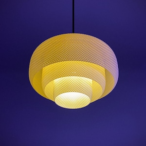 May include: A tiered pendant light fixture featuring a spherical shape with a fine, white mesh grid pattern. The structure consists of three concentric, circular layers that decrease in size toward the bottom, emitting a soft, warm yellow glow.