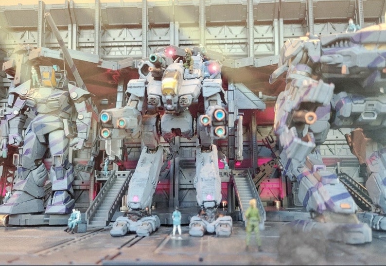 May include: Three large, gray, and white, robot-like figures stand in a hangar-like setting. The figures are made of plastic and have a futuristic design. The figures are posed in a battle-ready stance.