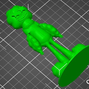 May include: Green 3D printed figurine of a cartoon character with a large head and a wide grin. The character has a large, round head with a wide, toothy grin. The body is made up of large, rounded limbs. The figurine is standing on a round base.