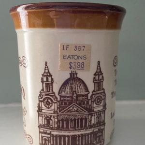 May include: A white ceramic mug with a brown rim and a brown illustration of a church. The mug has a price tag that reads "1F 367 EATON'S $3.98".