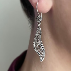 May include: Silver filigree earrings with a flower design at the top and a long, curved, teardrop-shaped pendant.