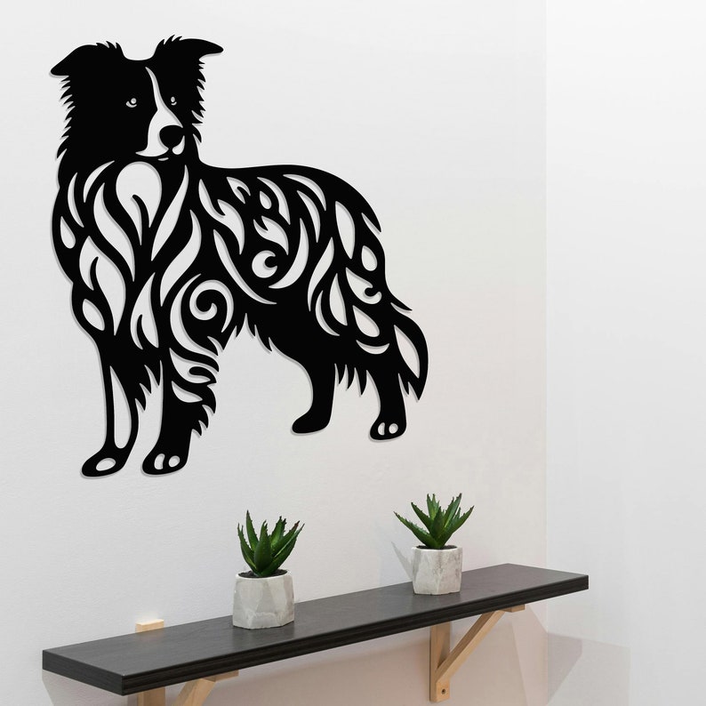 May include: Black and white silhouette of a border collie dog with intricate floral patterns cut out of the design. The dog is standing on a white wall with a wooden shelf below.