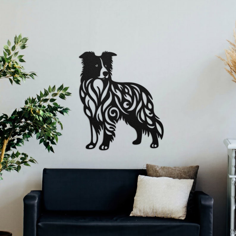 May include: Black silhouette of a border collie dog with intricate floral patterns cut out of the shape. The silhouette is mounted on a white wall above a black couch.