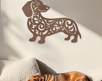 May include: A brown wooden dachshund silhouette wall decor with intricate floral patterns. The silhouette is mounted on a white wall. A real dachshund is sleeping on a white bed in the foreground.