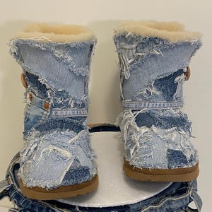May include: A pair of denim boots with a patchwork design. The boots have a light blue wash with distressed details and a tan sole. The interior is lined with a cream-colored, fluffy material. The boots are approximately 8 inches tall.