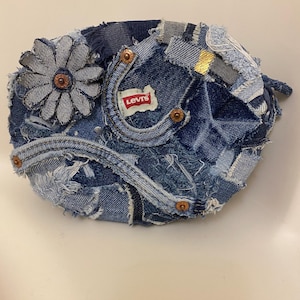 May include: A denim beret made from repurposed jeans. The hat features a flower applique, metal rivets, and a Levi's brand patch. The beret is a patchwork of different denim washes, creating a unique, textured look.