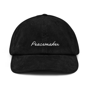 Puede incluir: Gorra de béisbol de pana negra con texto bordado en blanco que dice "Peacemaker".