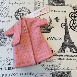 Puede incluir: Un conjunto de vestido y chaqueta de mu&ntilde;eca a cuadros rosas con botones perlados. La chaqueta tiene un cuello a juego con detalles de estrellas. El conjunto est&aacute; dise&ntilde;ado con un estilo cl&aacute;sico, perfecto para el guardarropa de una mu&ntilde;eca.
