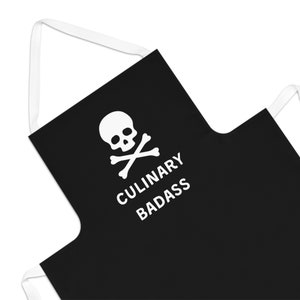 May include: Black apron with white skull and crossbones graphic and the text "CULINARY BADASS". The apron has white straps and is designed for kitchen use. A fun and edgy accessory for cooking enthusiasts.