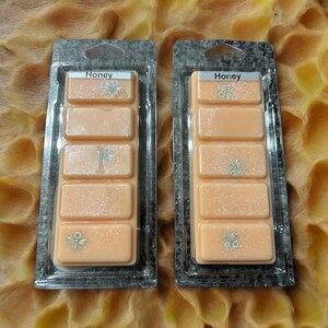 May include: Two clear plastic packages containing wax melts. Each package has five wax melt cubes with a light peach color and a glittery finish. The wax melts are labeled "Honey".