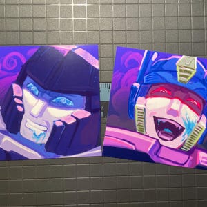 Peut inclure: Deux impressions d'art carrées représentant des visages de robots stylisés. L'une a un casque bleu foncé et un visage blanc avec des accents bleus. L'autre a un casque bleu, un visage blanc et des accents rouges. Les deux ont un fond violet et rose.