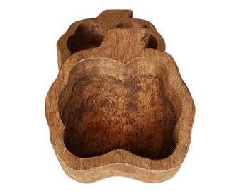 May include: A hollowed-out wooden bowl shaped like an apple with a natural brown finish and visible wood grain texture. The bowl features a stem-like protrusion at the top and a deep, rounded interior cavity, showcasing a rustic, carved appearance.