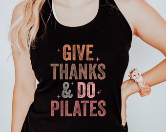 May include: Black vest top with the text "GIVE THANKS & DO PILATES" in orange, brown, and pink lettering. The vest top is sleeveless and has a scoop neck. The word "BLACK" is printed in the bottom right corner.