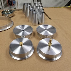 May include: A set of four silver metal caps with a small brass fitting on two of the caps. The caps are on a brown surface.