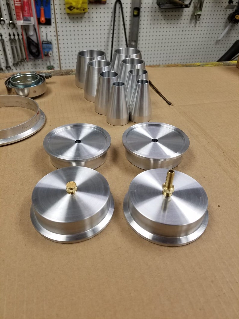 May include: A set of four silver metal caps with a small brass fitting on two of the caps. The caps are on a brown surface.