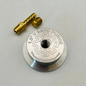 May include: A silver 1.5" V-band purge fitting with a threaded hole in the center. The fitting is labeled "1.5" V-band Purge" and "WilsonMachining.com".