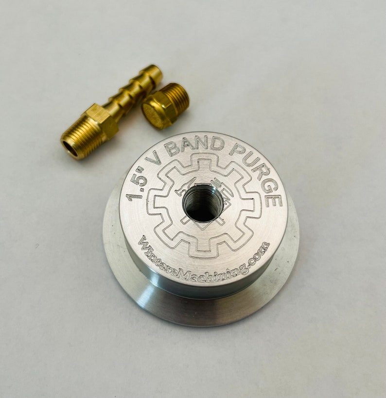 May include: A silver 1.5" V-band purge fitting with a threaded hole in the center. The fitting is labeled "1.5" V-band Purge" and "WilsonMachining.com".