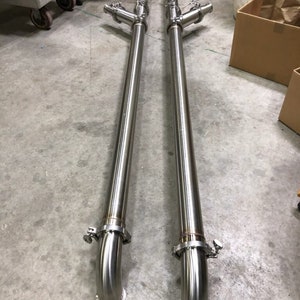 May include: Two long, silver, stainless steel pipes with a 90-degree bend at the bottom. Each pipe has a T-shaped connector with two smaller pipes branching off at a 90-degree angle.