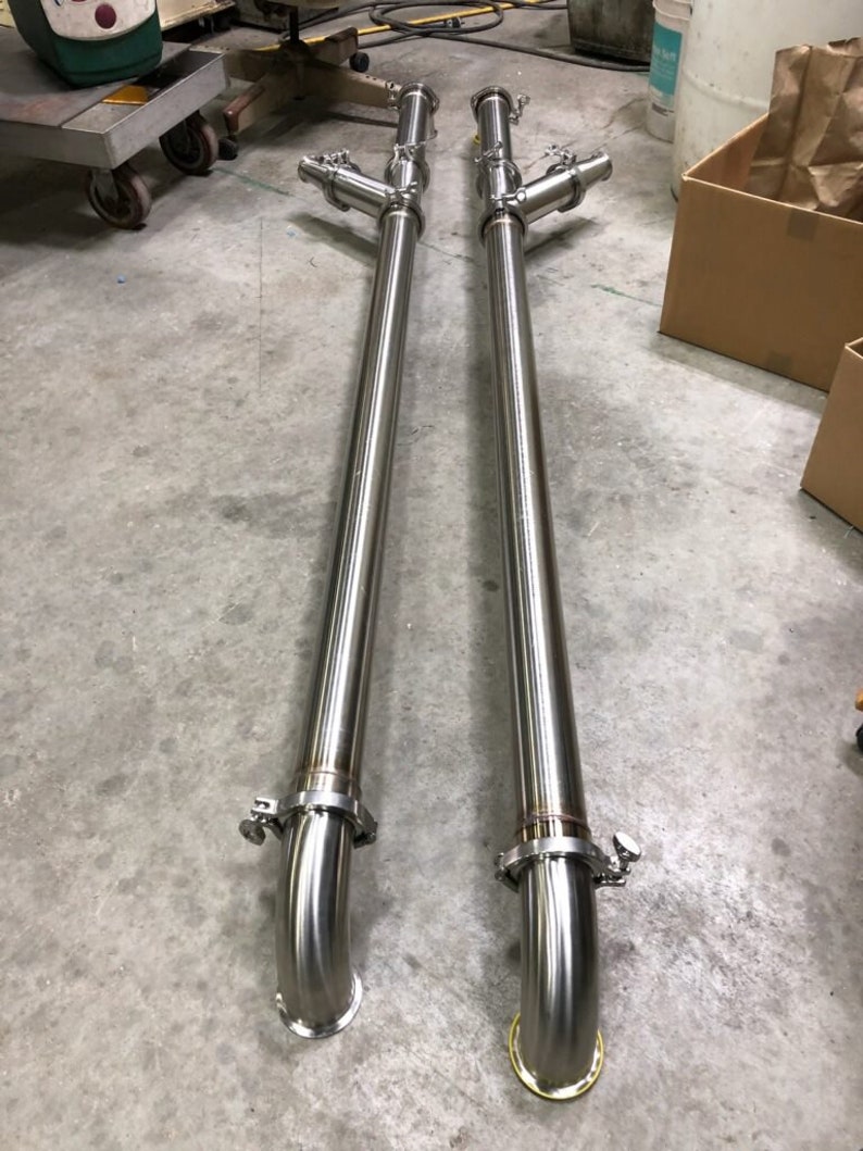 May include: Two long, silver, stainless steel pipes with a 90-degree bend at the bottom. Each pipe has a T-shaped connector with two smaller pipes branching off at a 90-degree angle.