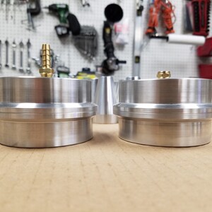 May include: Two silver metal cylinders with a brass fitting on top. The cylinders are stacked on top of each other and have a smooth, polished finish.