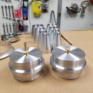 May include: Two silver metal caps with a brass fitting on top. The caps are sitting on a brown surface.