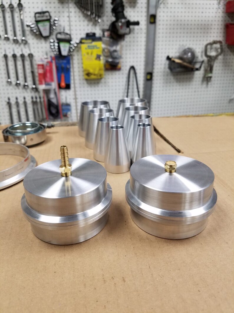 May include: Two silver metal caps with a brass fitting on top. The caps are sitting on a brown surface.