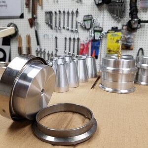 May include: A set of silver metal parts for a machine. The parts include a round disc with a hole in the center, a ring with a lip, and several cone-shaped pieces.