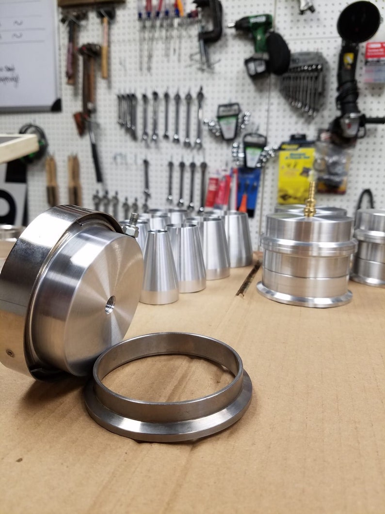 May include: A set of silver metal parts for a machine. The parts include a round disc with a hole in the center, a ring with a lip, and several cone-shaped pieces.