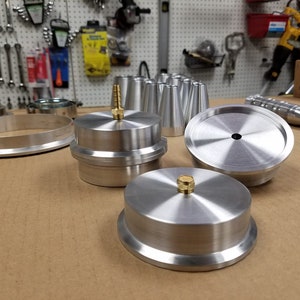 May include: A set of silver metal parts for a machine, including a round ring, a round disc with a hole in the center, and a round disc with a small brass knob on top.