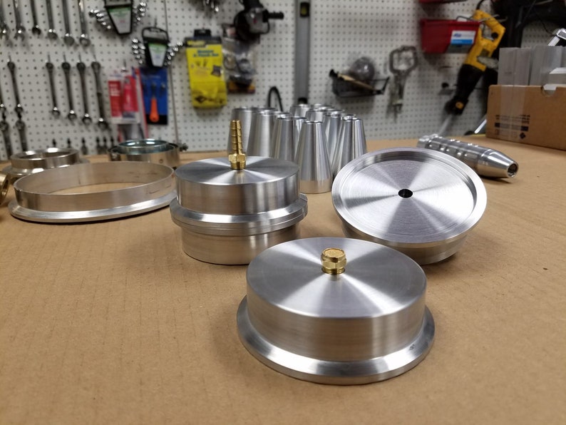 May include: A set of silver metal parts for a machine, including a round ring, a round disc with a hole in the center, and a round disc with a small brass knob on top.